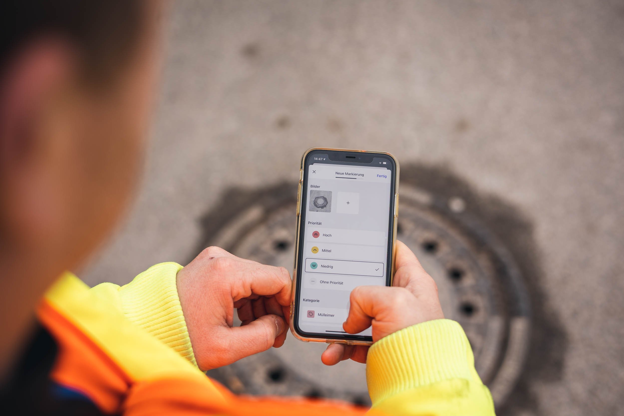 Bauhof Mitarbeiter erstellt eine neue Aufgabe von einem Schachtdeckel mit Handy in der Hand